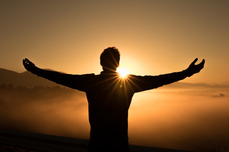 Silhouette of a person with arms outstretched facing a golden sunrise over a misty mountain valley